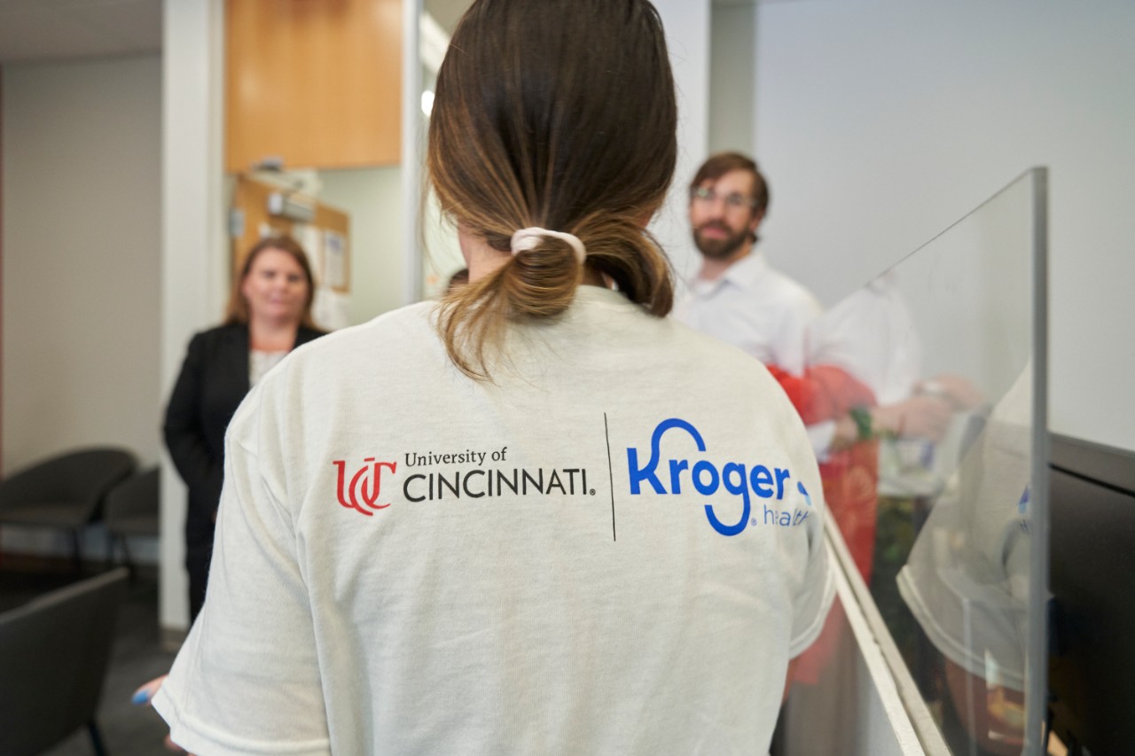 A student wears a shirt with a University of Cincinnati logo and a Kroger logo