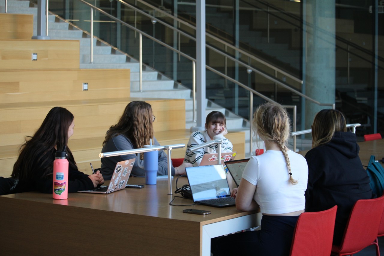 Students at a long wooden table in the Atrium of the Health Sciences Building. 